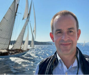 Yves Pointel devant la mer Méditerranée, avec un bateau à voile dans le fond
