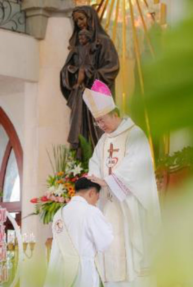 un des jeunes vietnamiens à genou devant l'évêque qui lui impose les mains