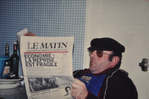 Lucien, ouvrier, casquette sur la tête, lit le journal, assis dans son fauteuil